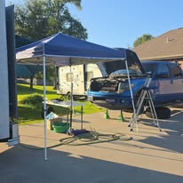A vehicle with its hood open beneath a portable canopy in a driveway